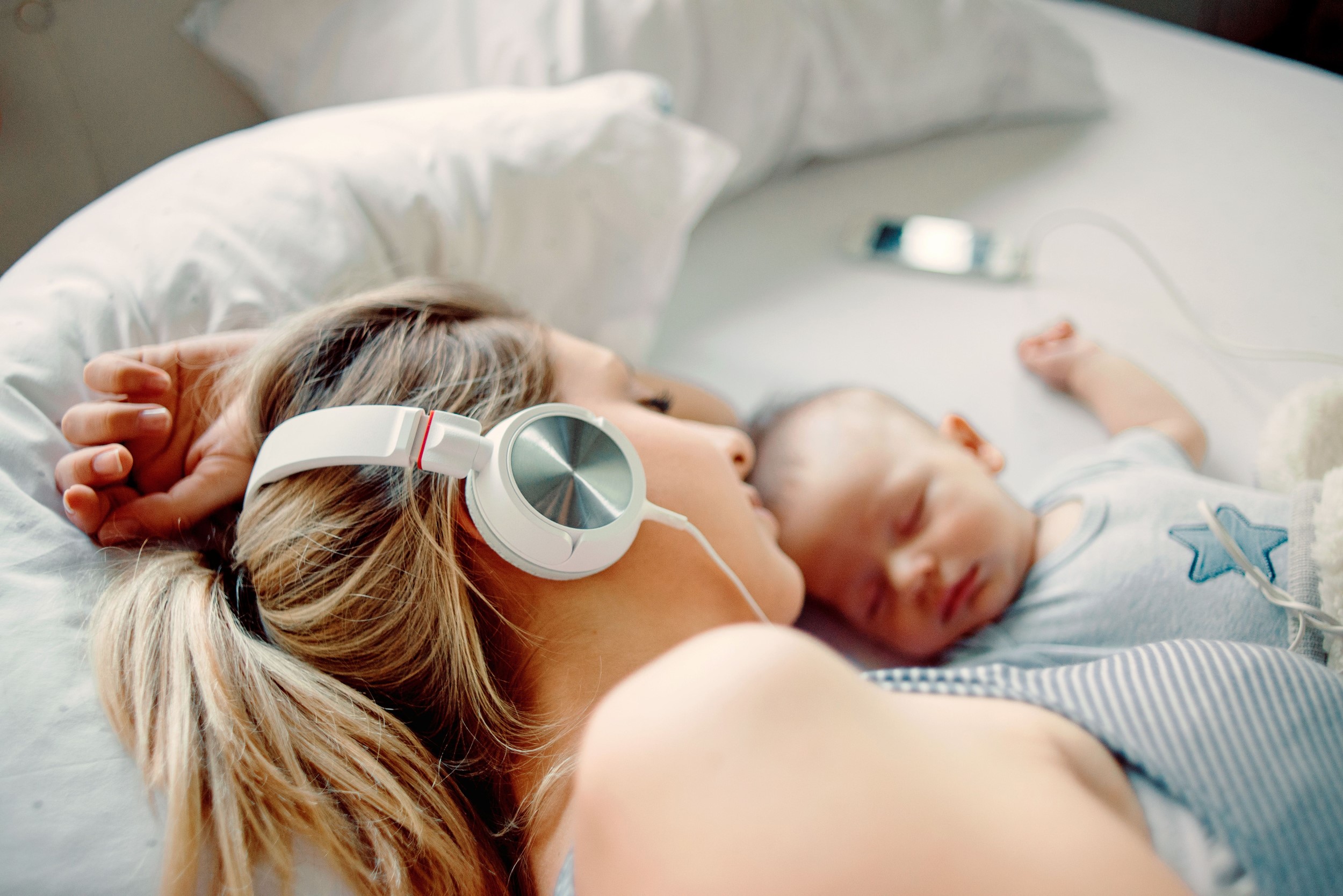 Woman lying next to hear newborn, listening to a postpartum affirmations MP3