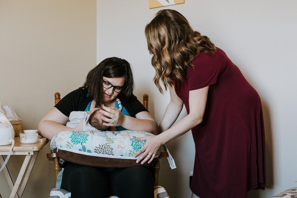 A mother feeds her newborn while a postpartum doula provides one-on-one feeding support